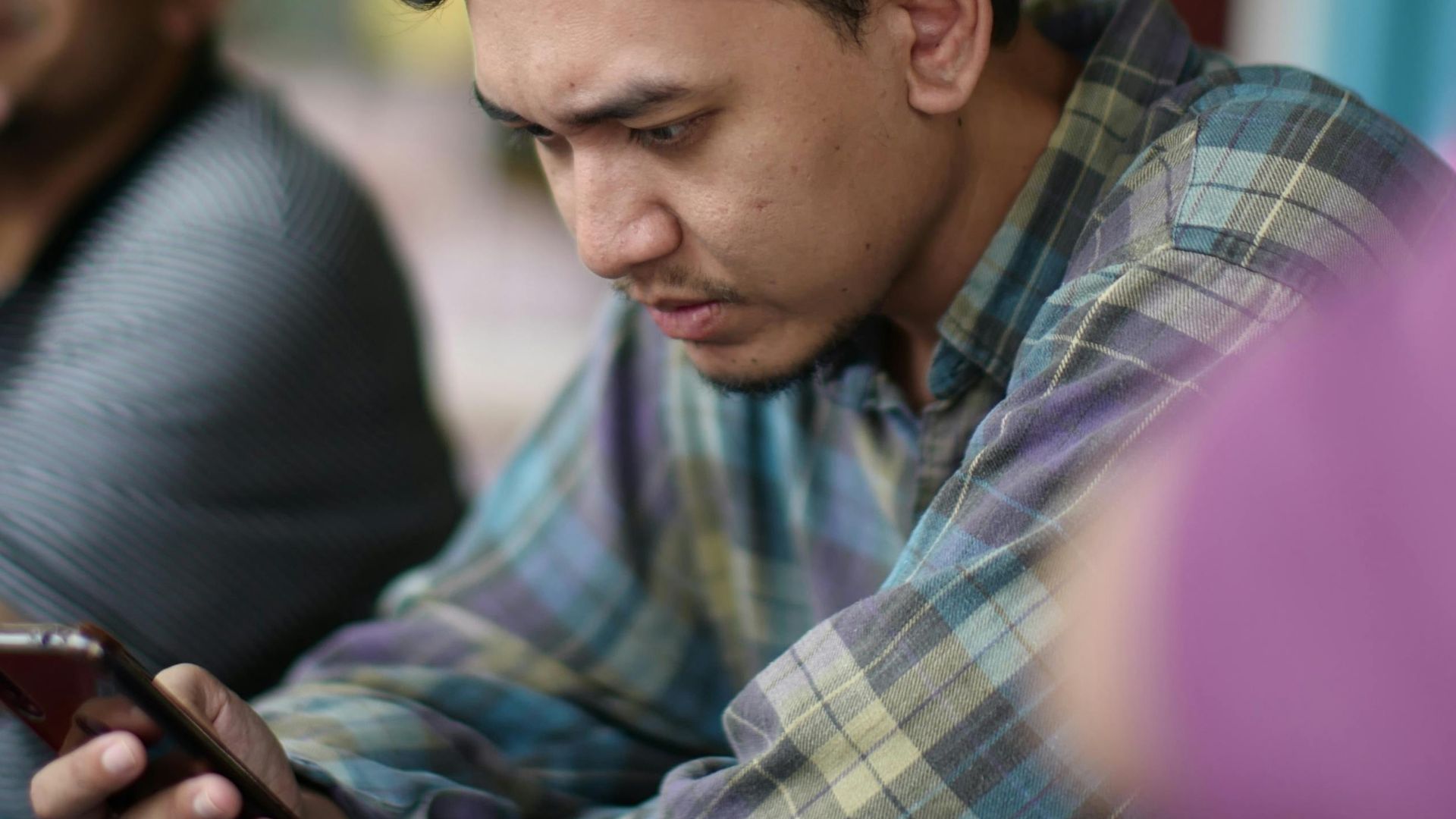 Young man focused on smartphone in a lively Kuala Dungun cafe setting.