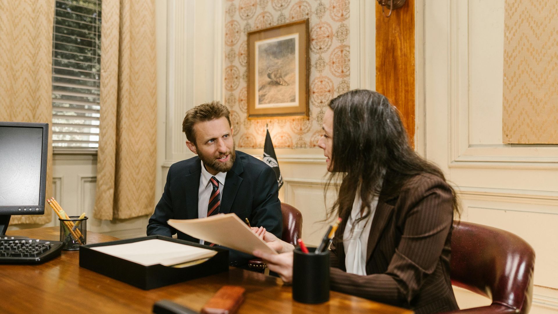 Two professionals engaged in a business discussion in an office setting, reviewing legal documents.