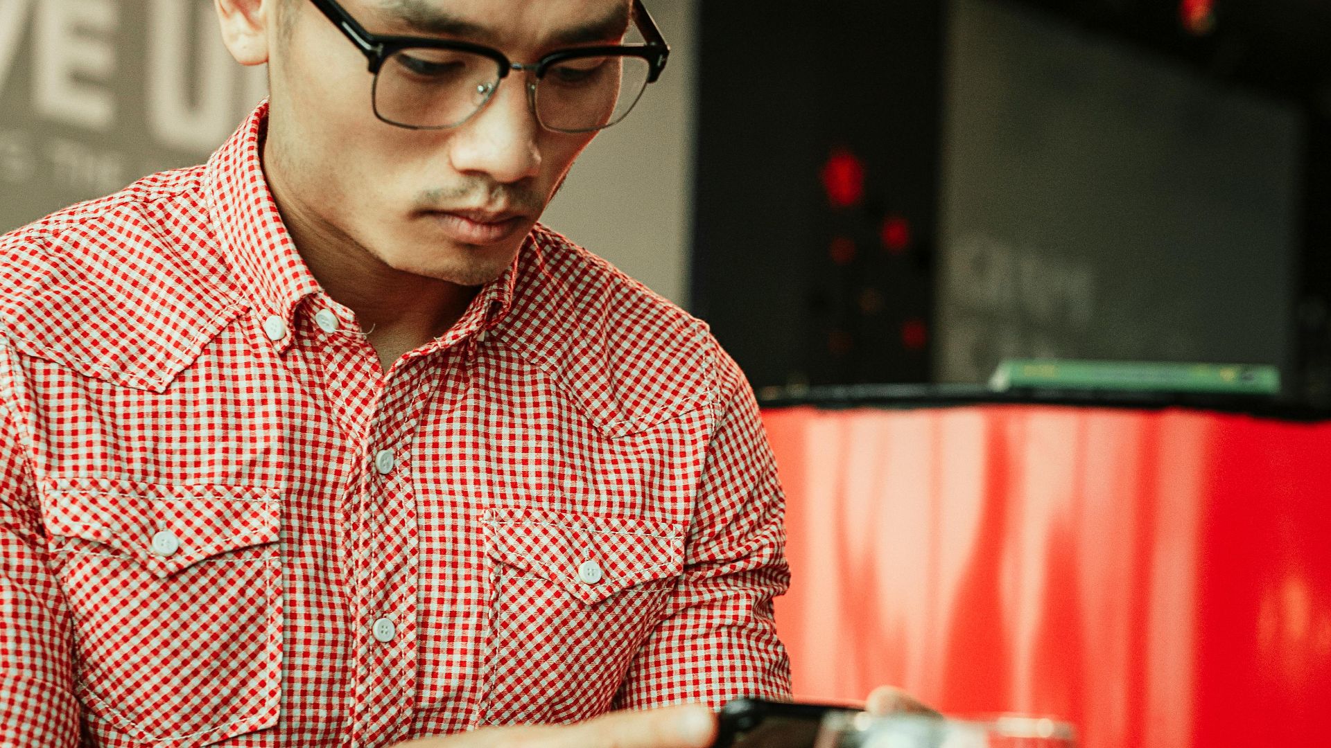 Man wearing glasses focused on using smartphone indoors with a modern setting.
