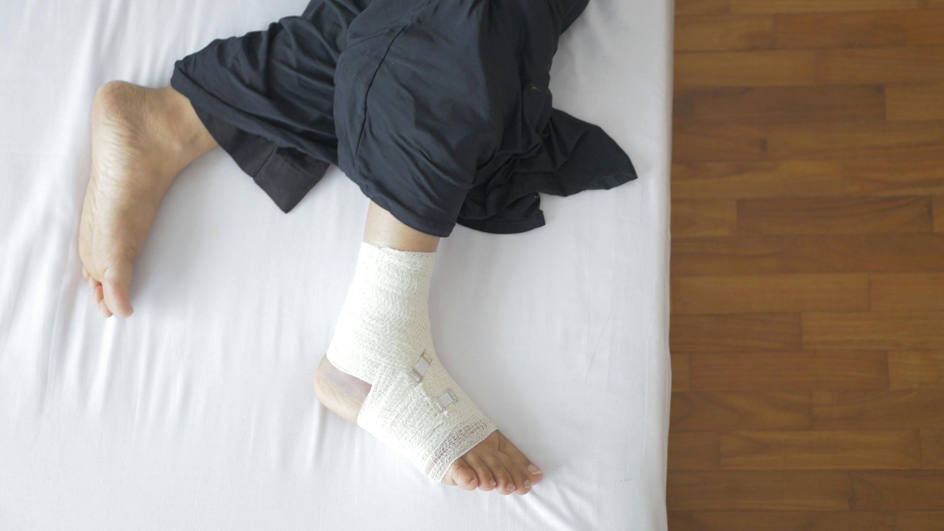 Top view of a bandaged foot resting on a bed, depicting injury and recovery.