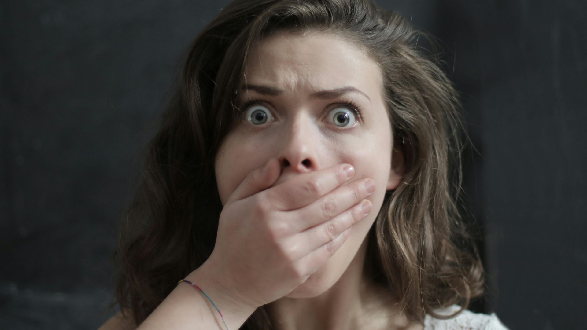 Close-up of a woman with a shocked expression, covering her mouth with her hand. Emotional and intense moment.