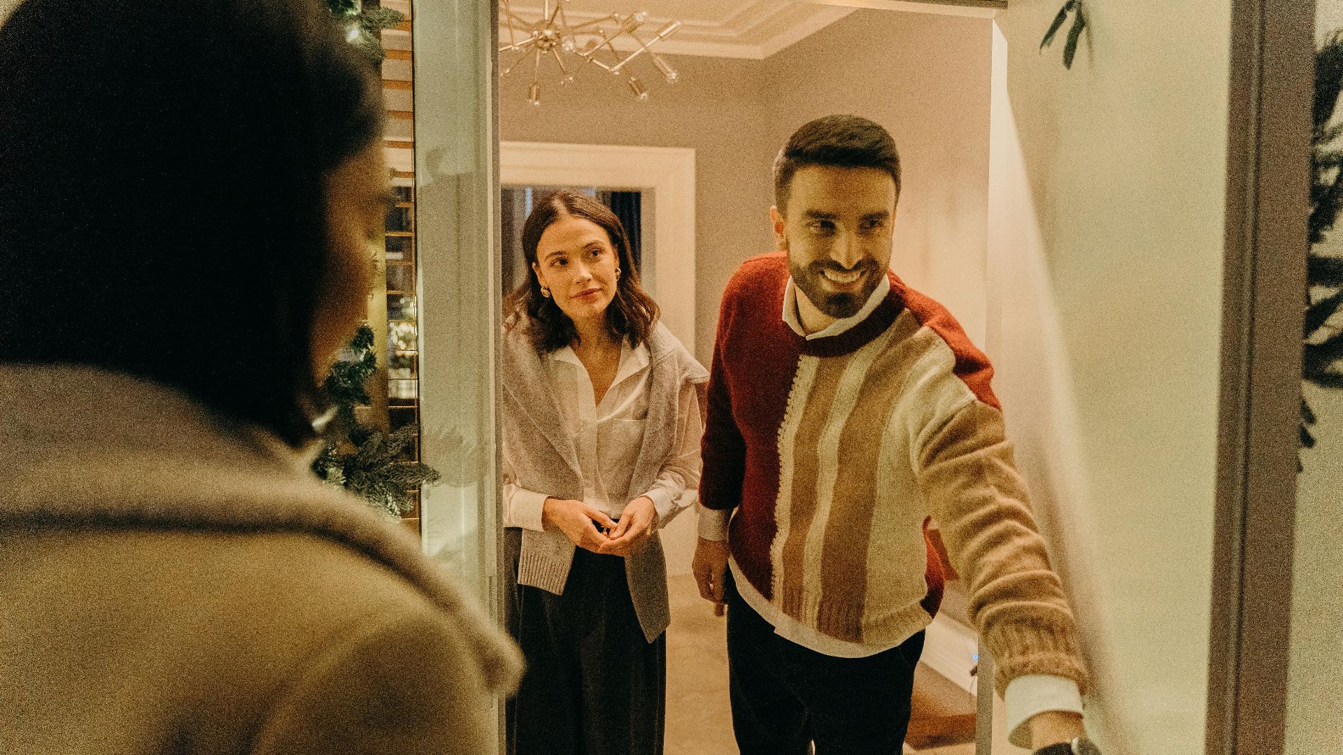 A couple greeting a guest at their doorway, capturing the warmth of a home during the holiday season.