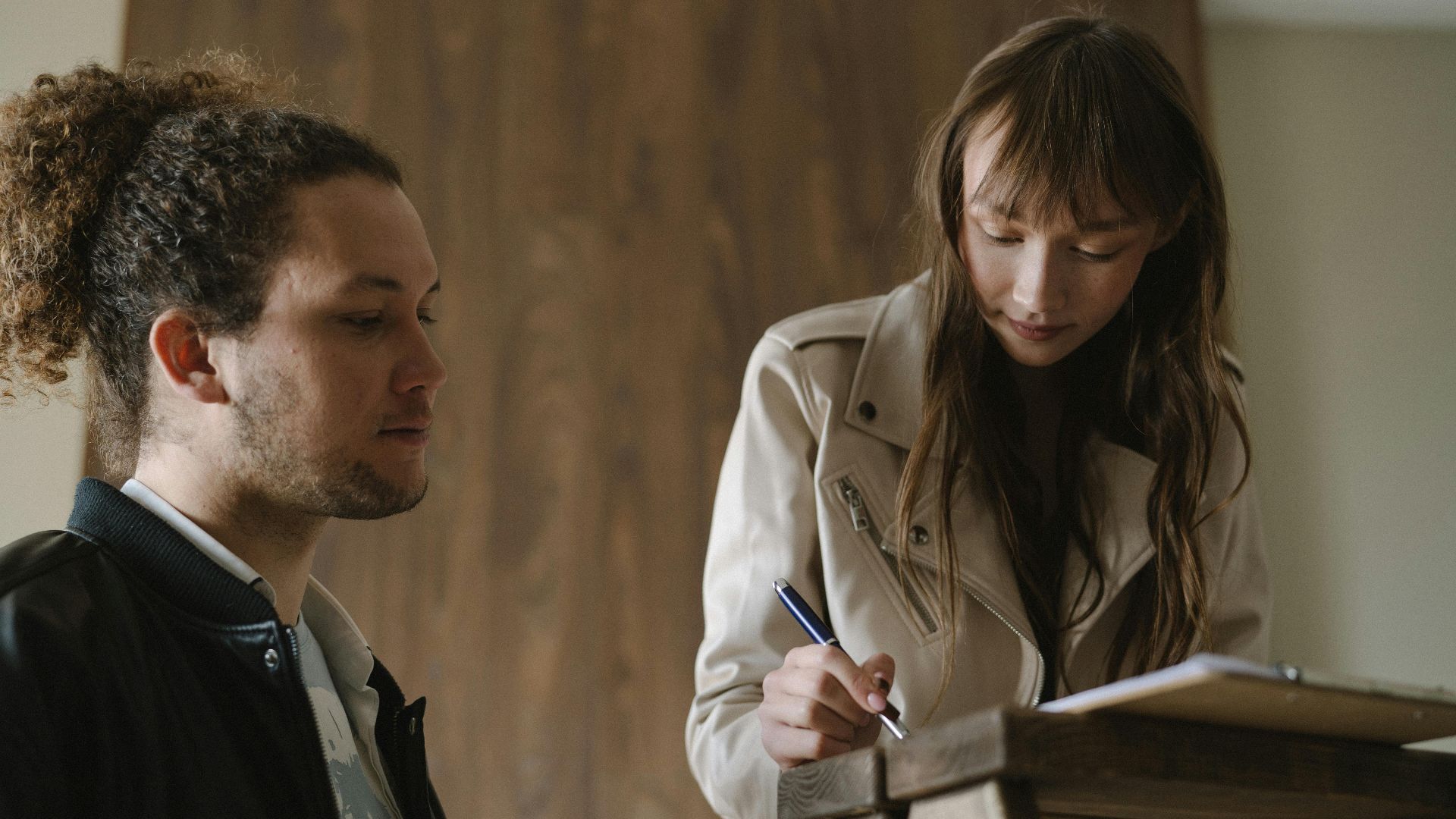 A young couple reviews and signs real estate documents indoors.
