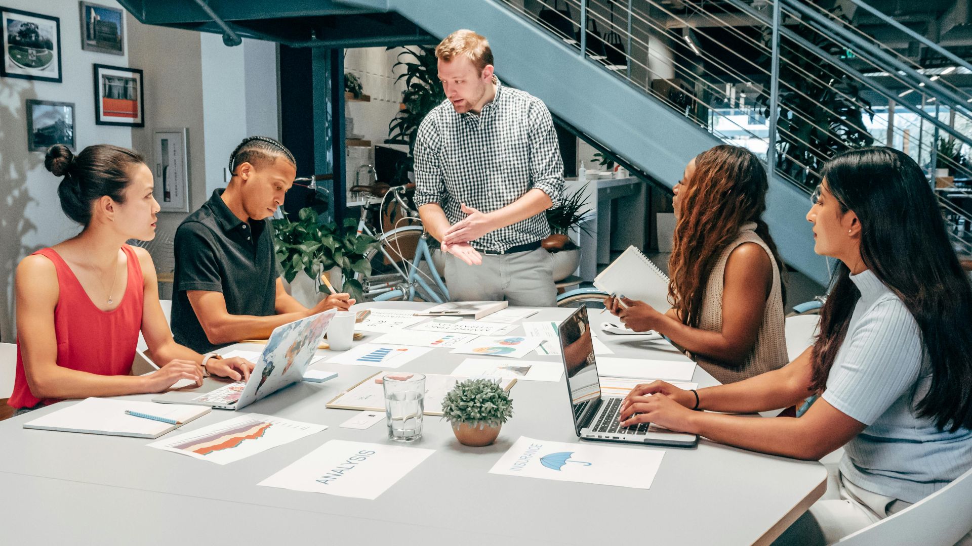 A diverse group of colleagues collaborating on a project in a modern office setting with laptops and documents.