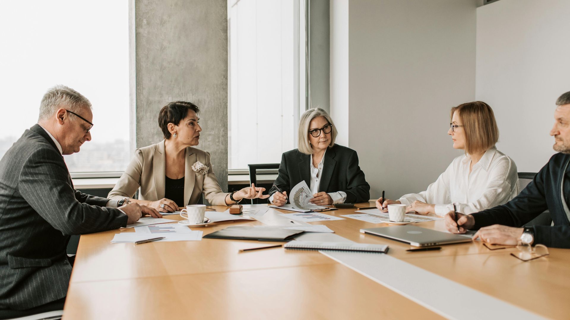 Five business professionals engaged in a meeting in a modern office setting, discussing documents and ideas.