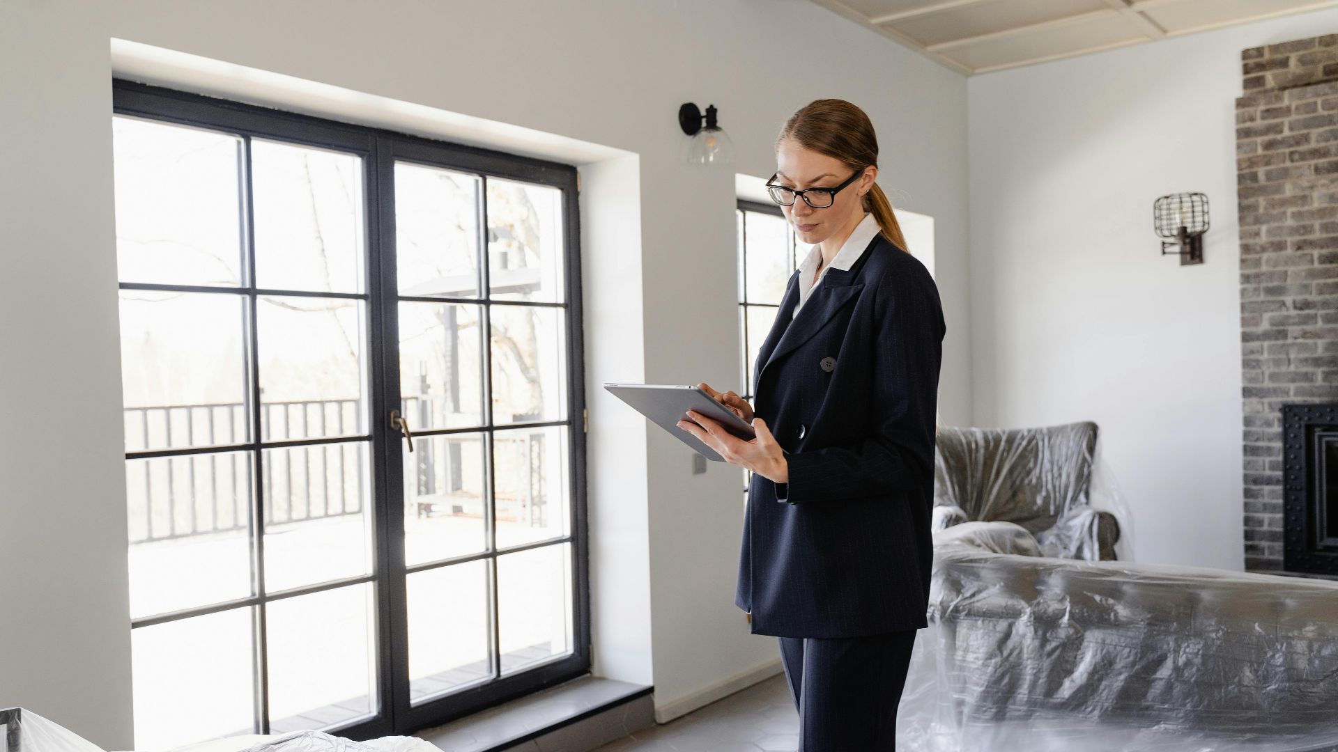 Real estate agent in a black blazer using a tablet inside a furnished home.