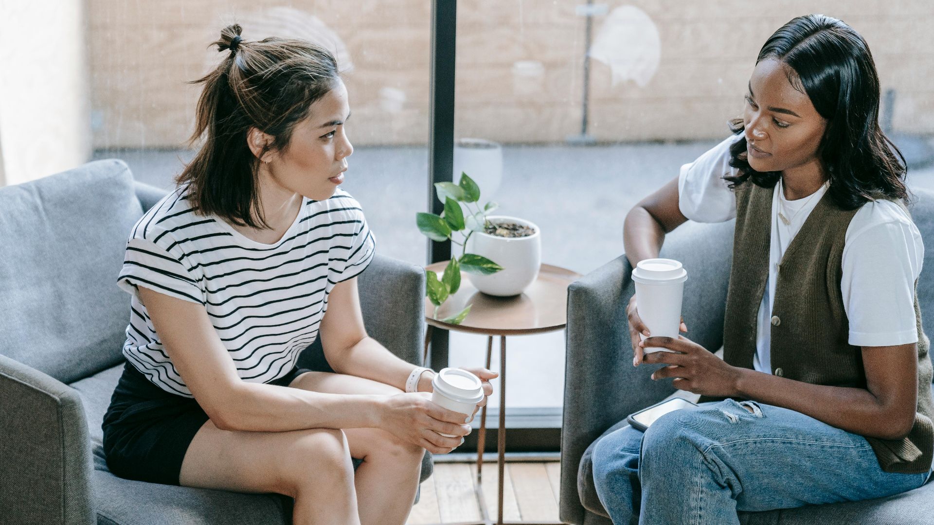 Two young women enjoying coffee and conversation indoors in a cozy setting.