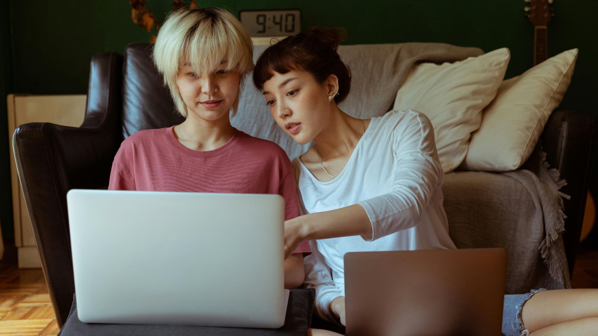 Young Asian female friends using laptops while working on collaborative project on floor in room