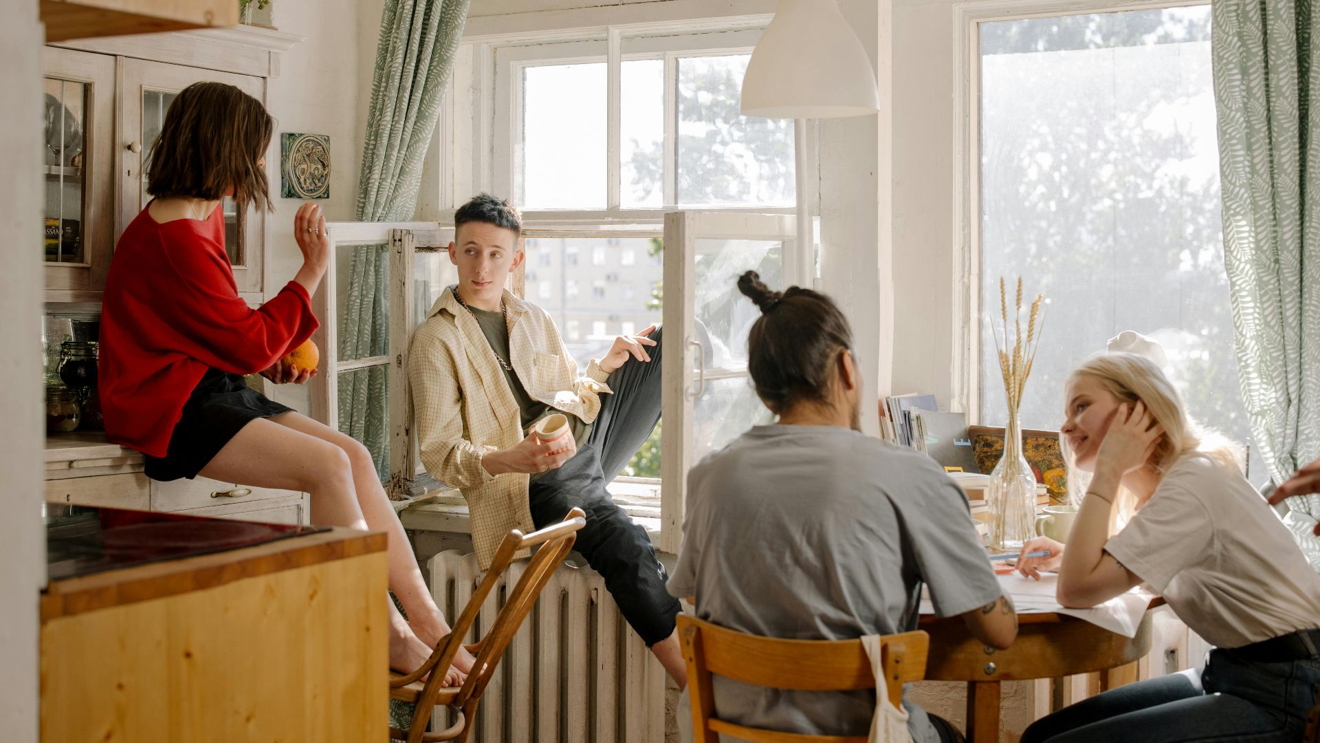 Group of young friends relaxing and chatting in a sunlit kitchen space.
