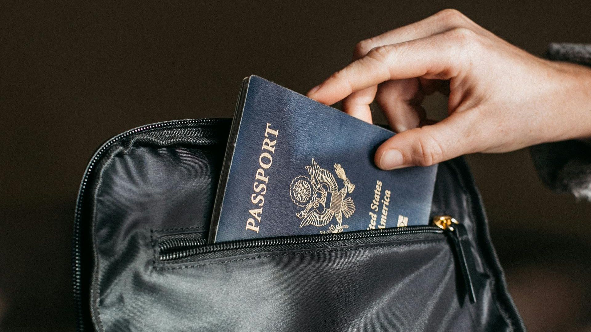 Close-up of a person placing a passport into a leather bag, ready for travel.