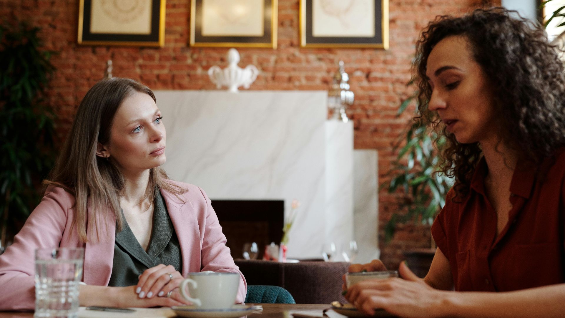 Two women engaged in serious discussion over coffee in a cozy indoor cafe setting.
