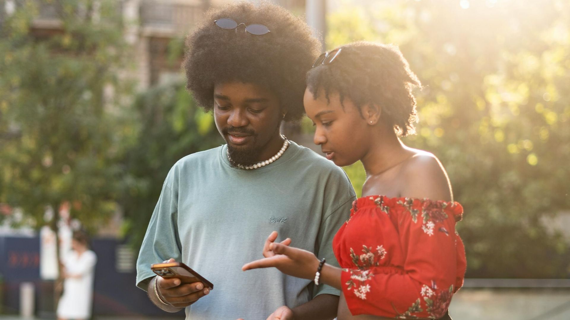 A young couple standing together at a bus stop, engaged with a smartphone in an urban setting, capturing a moment of connection and technology.