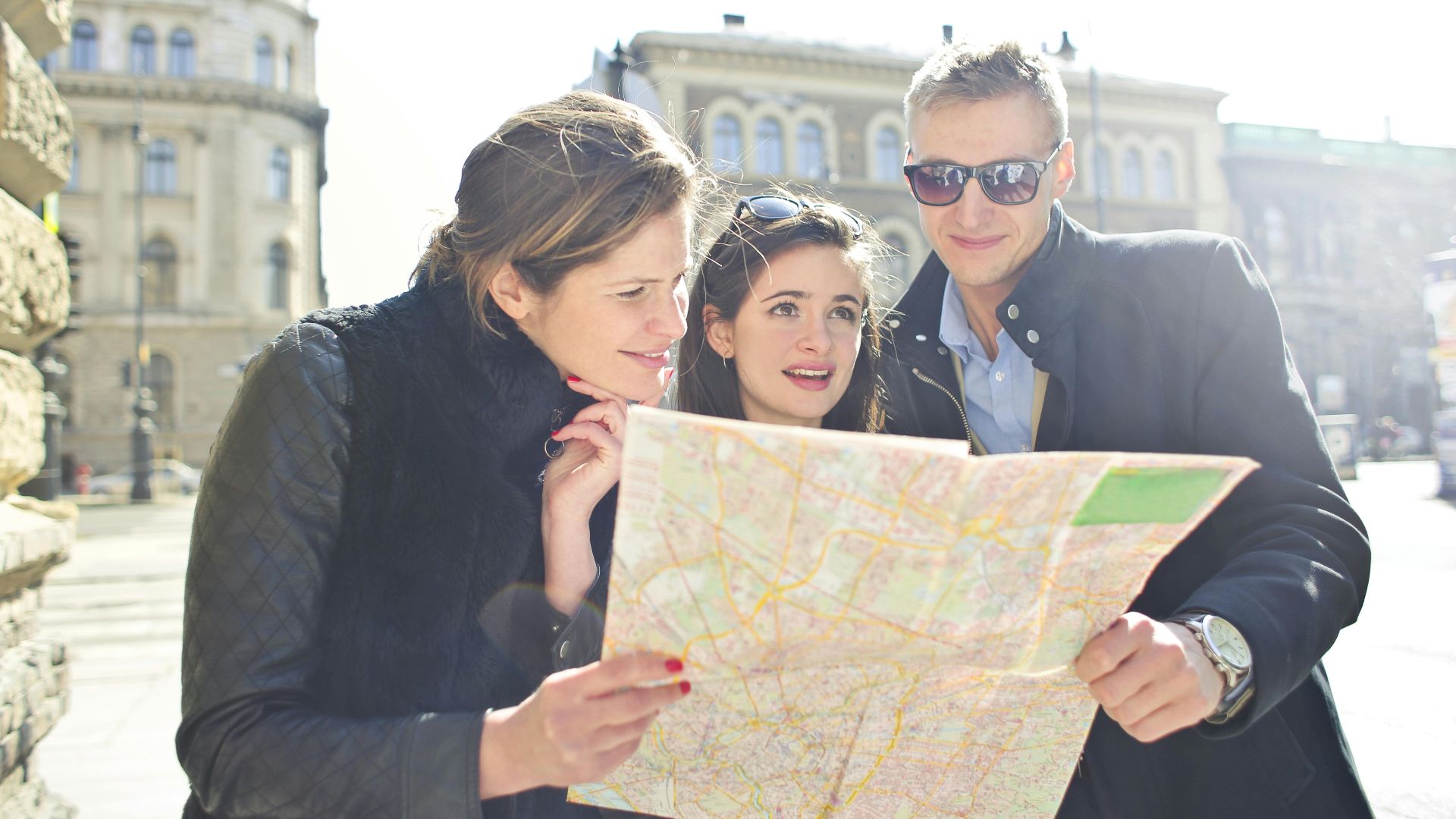 Three tourists exploring a city using a map under bright daylight, enjoying their travel journey.