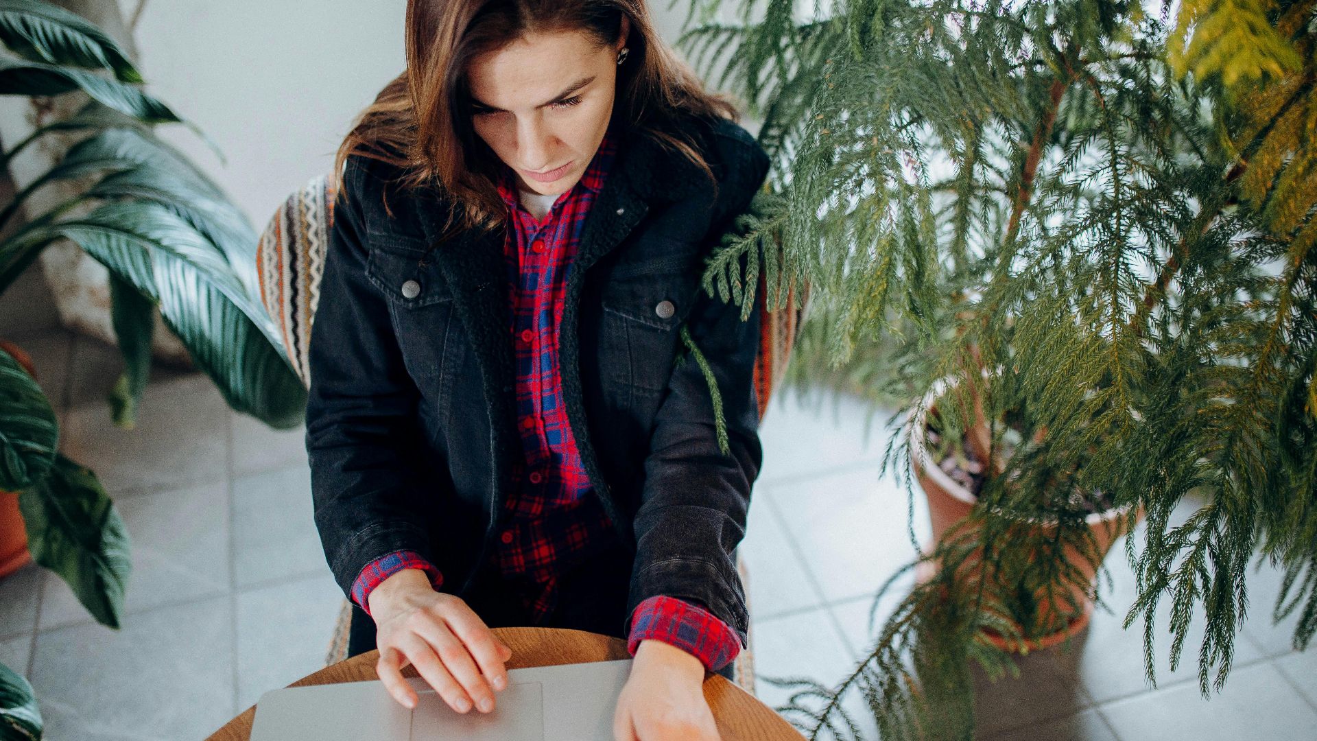 A young woman using a laptop surrounded by plants provides a natural workspace vibe.