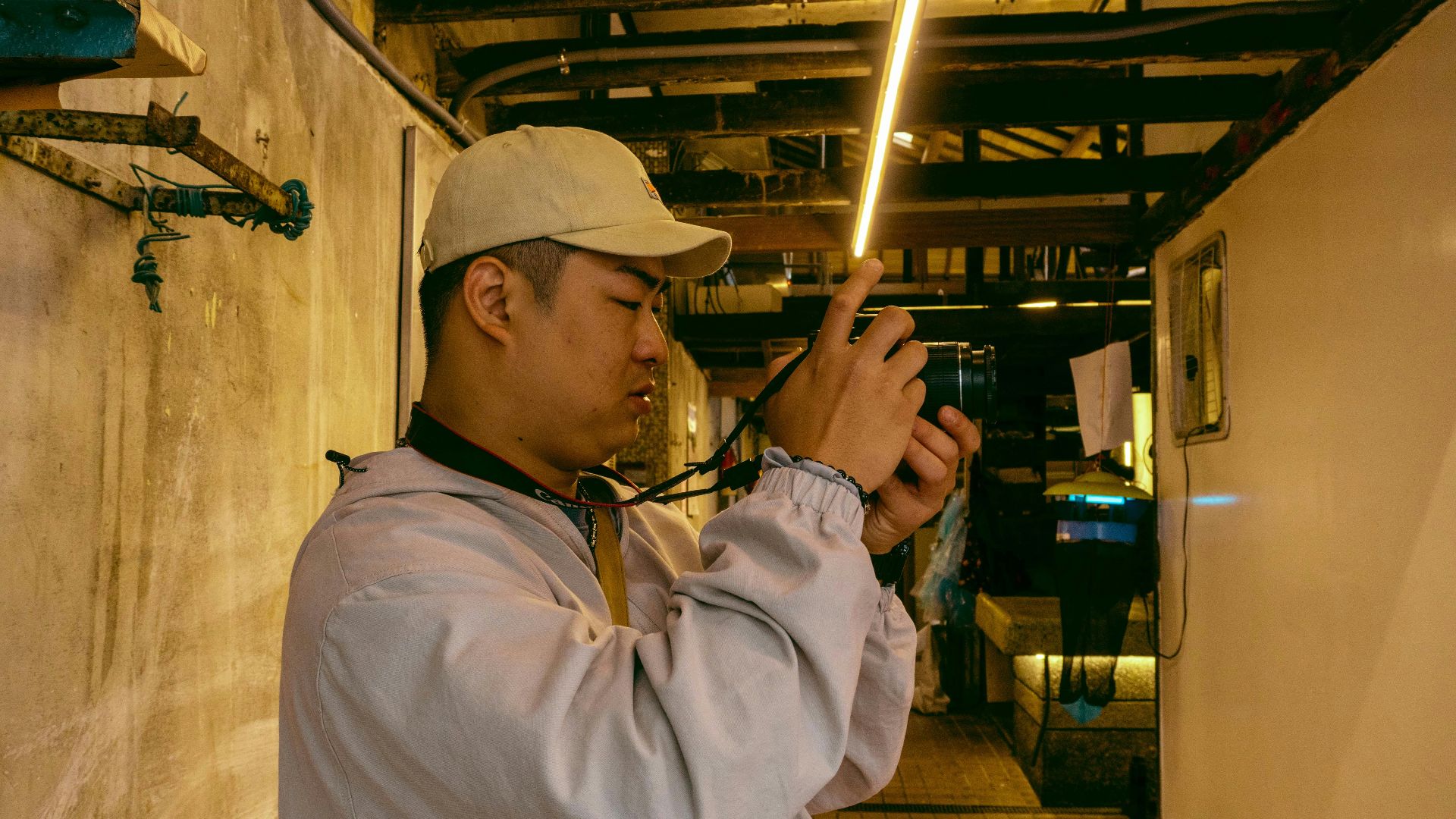 Man in cap photographing indoors with a compact camera under warm lights.
