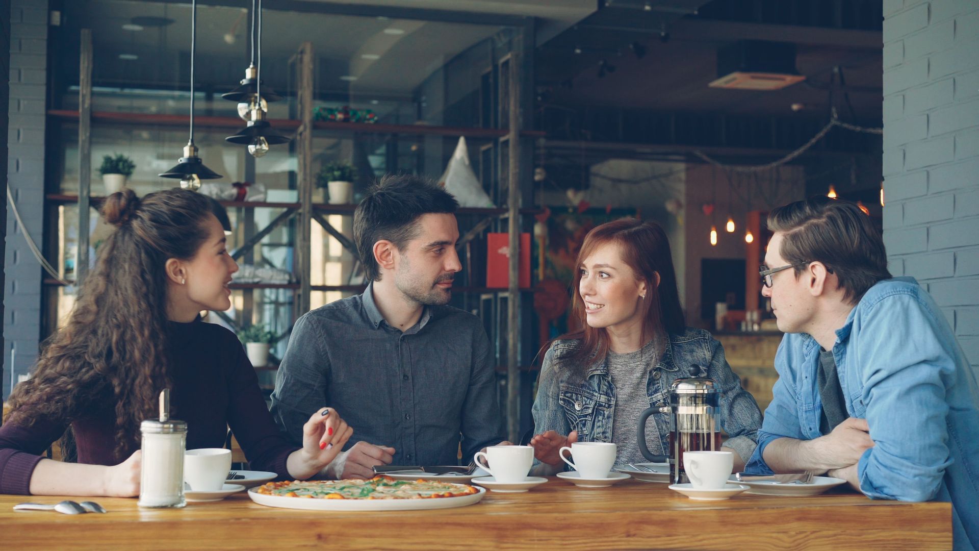 A group of adults having coffee and pizza at an indoor cafe setting.