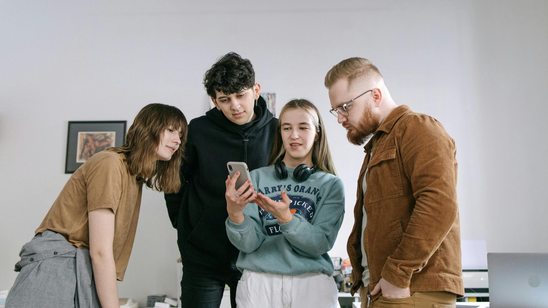 Group of young adults reviewing content on a smartphone in an office setting.