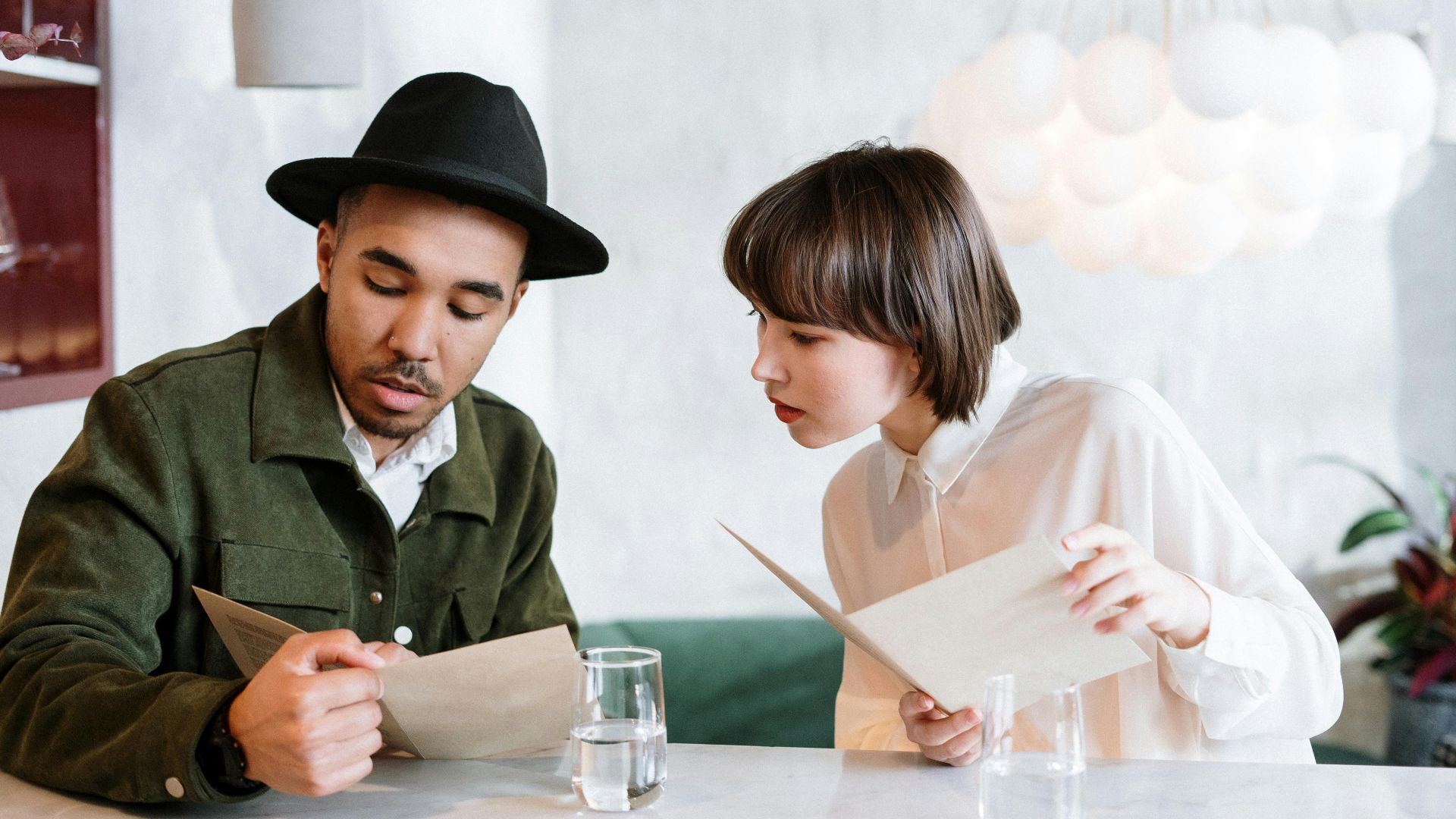 A couple reviews the menu in a modern cafe setting, discussing their meal choices.