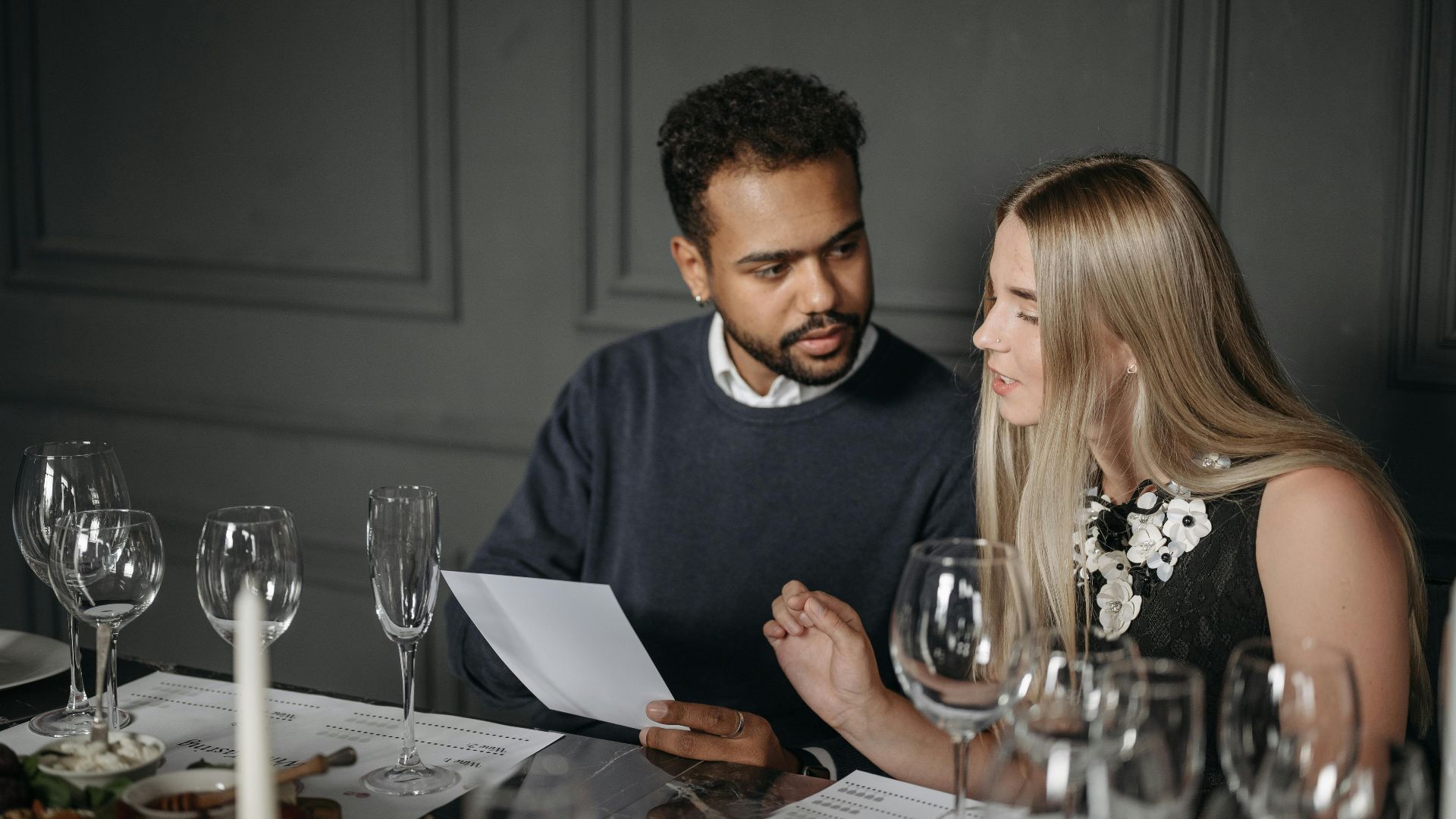 A man and woman engaged in a wine tasting discussion, seated at an elegantly set table.