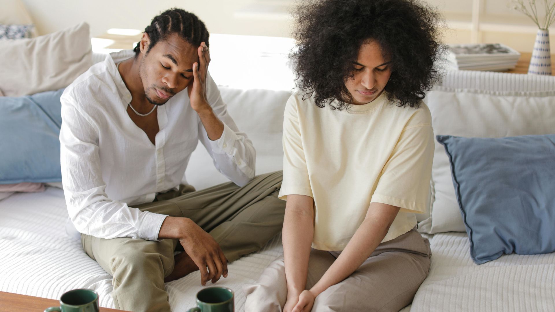 A contemplative black couple sitting on a sofa indoors in a modern setting, reflecting emotions.