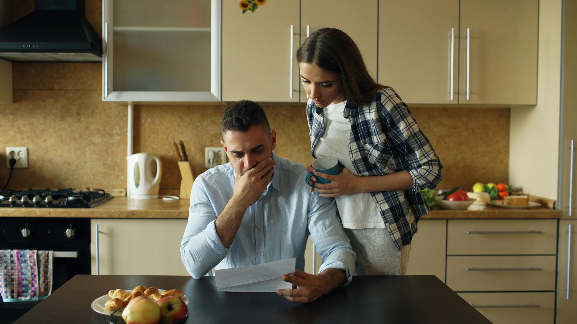 Concerned couple reviewing financial document in modern kitchen setting.