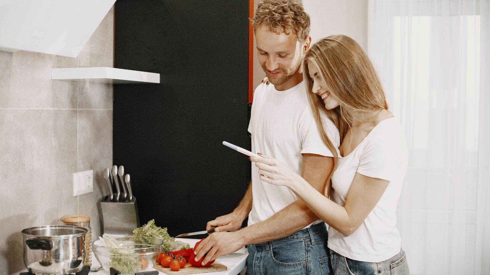 Couple happily preparing a healthy meal together in a modern kitchen setting.