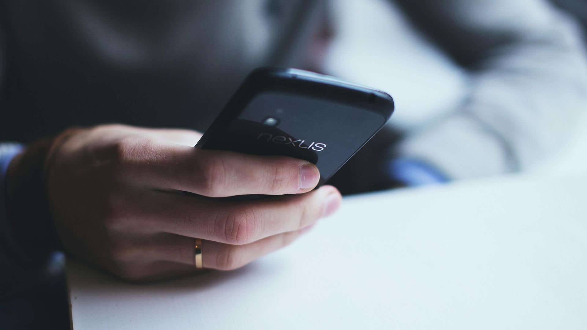 Close-up of a person holding a smartphone while sitting at a white table.