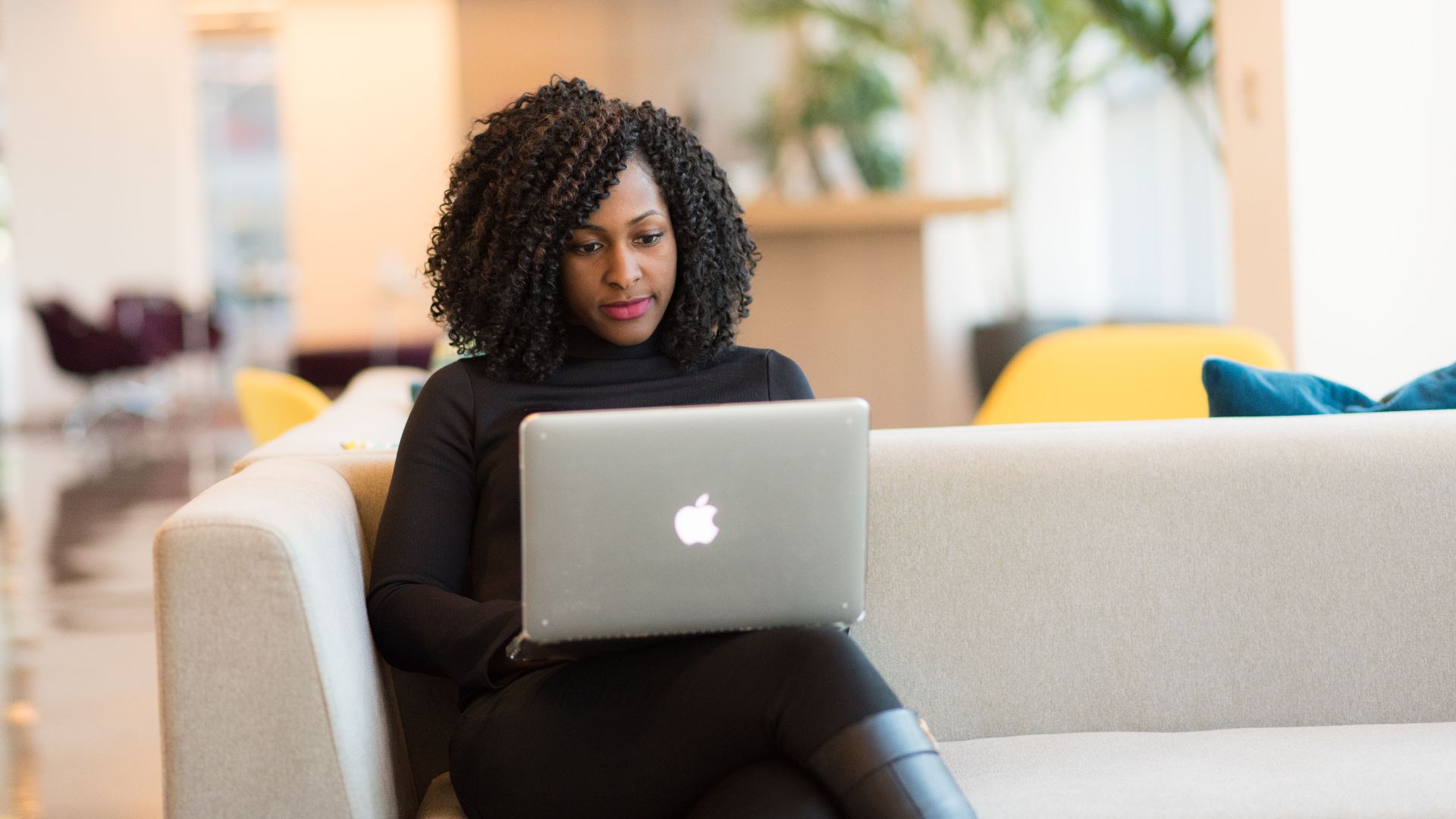 An African American woman working remotely on a laptop in a modern indoor setting.