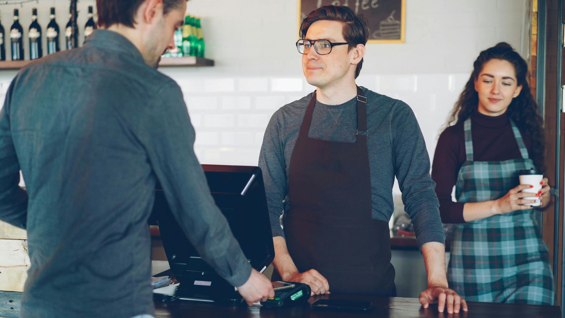 Casual interaction at a coffee shop counter with barista and customers.