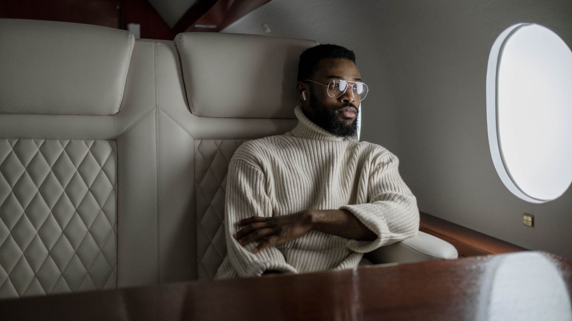 A stylish man in a turtleneck relaxes inside a private jet, embodying luxury travel.