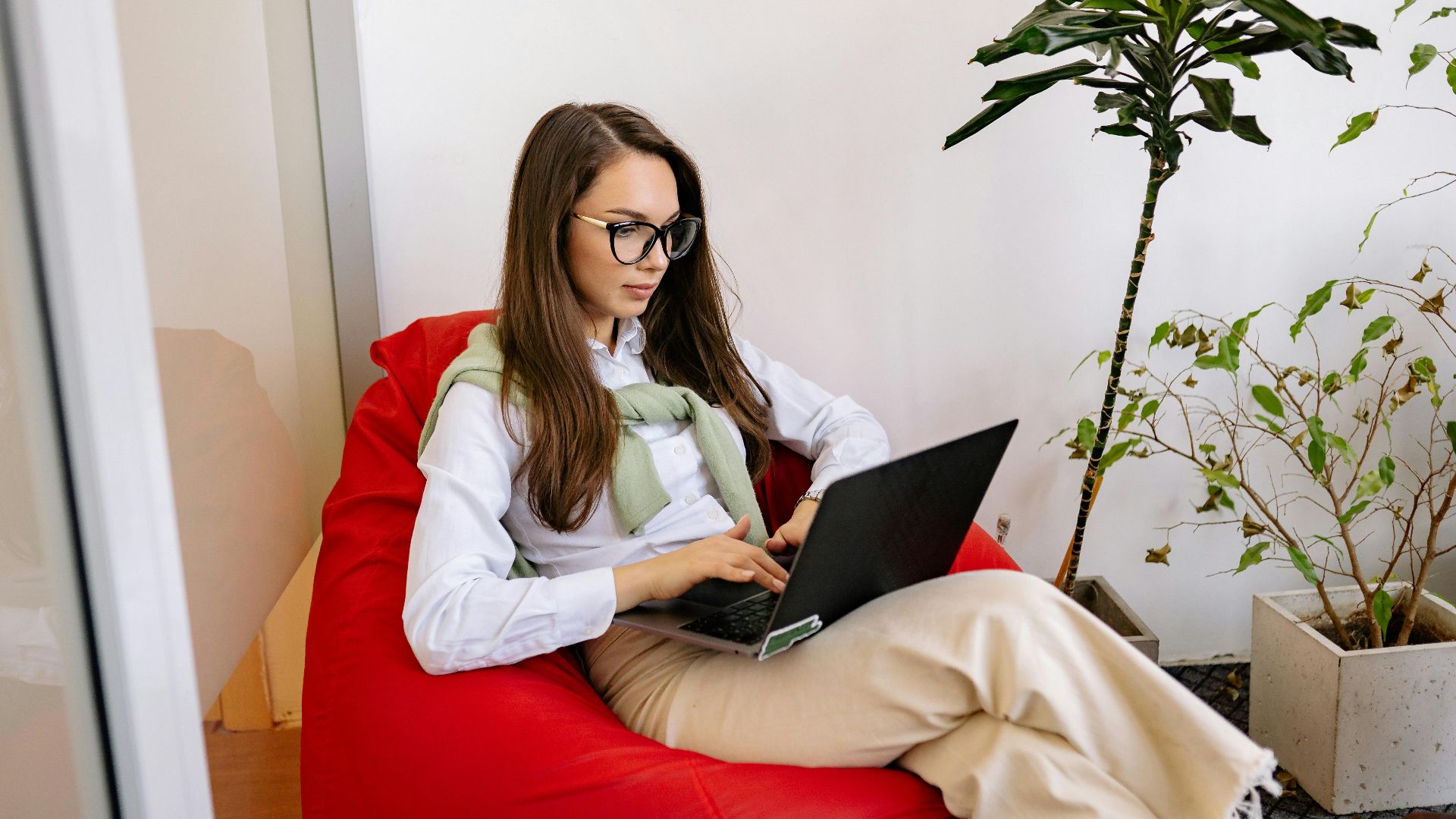 Woman working on laptop while relaxing in a bean bag in modern indoor setting.