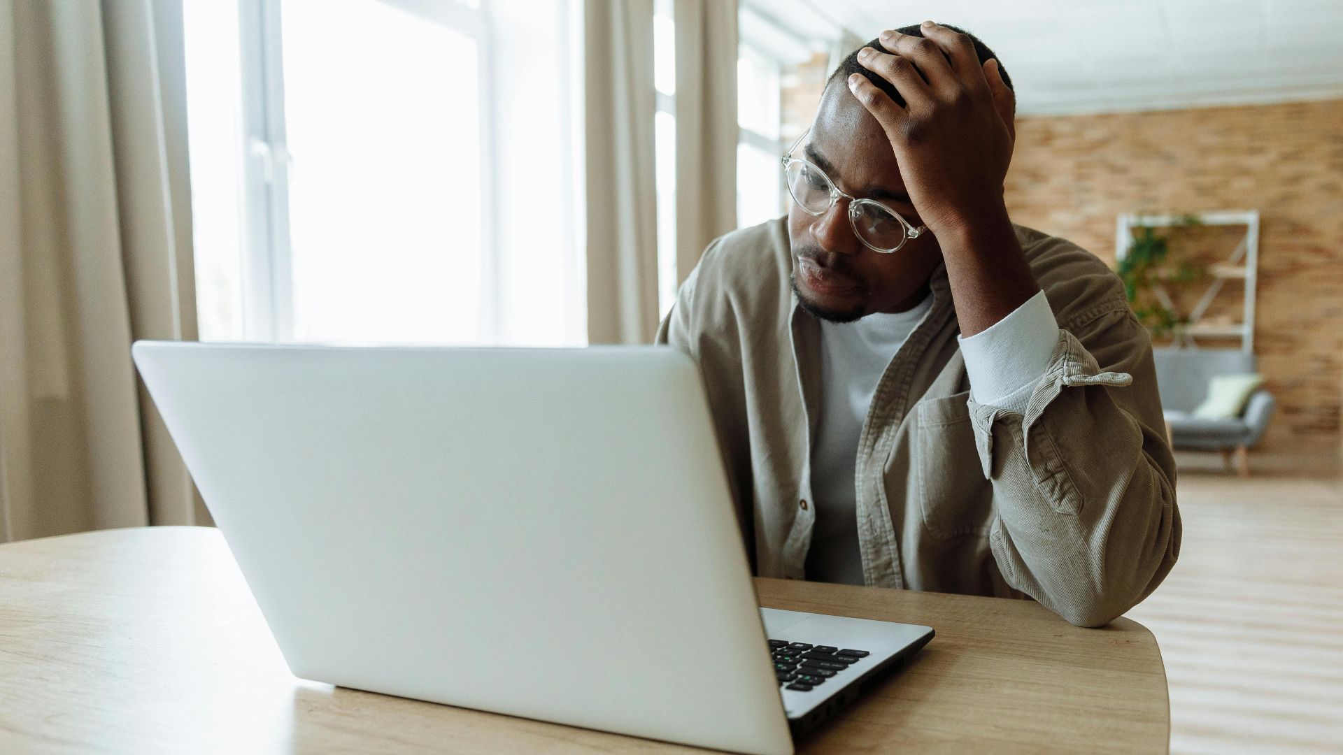Man stressed while working on a laptop indoors, dealing with issues in remote work.