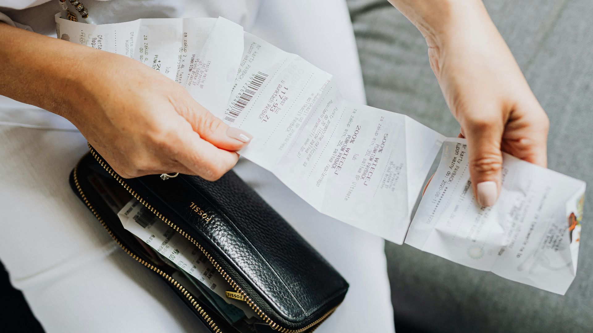 Close-up of a woman's hands managing multiple receipts taken from a black wallet.