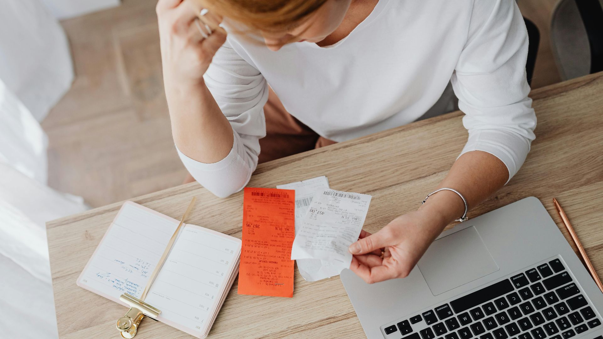 Woman reviewing receipts and planning budget using a laptop and notebook at home to manage expenses.
