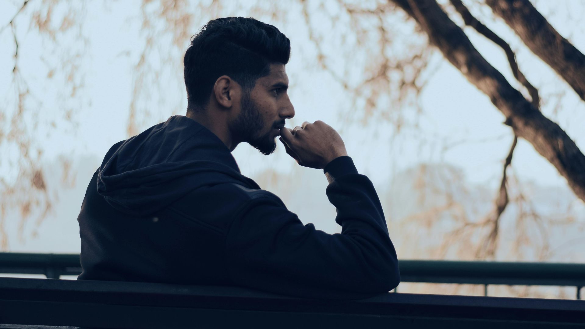 Man in deep thought sitting on a bench in a serene autumn park setting.