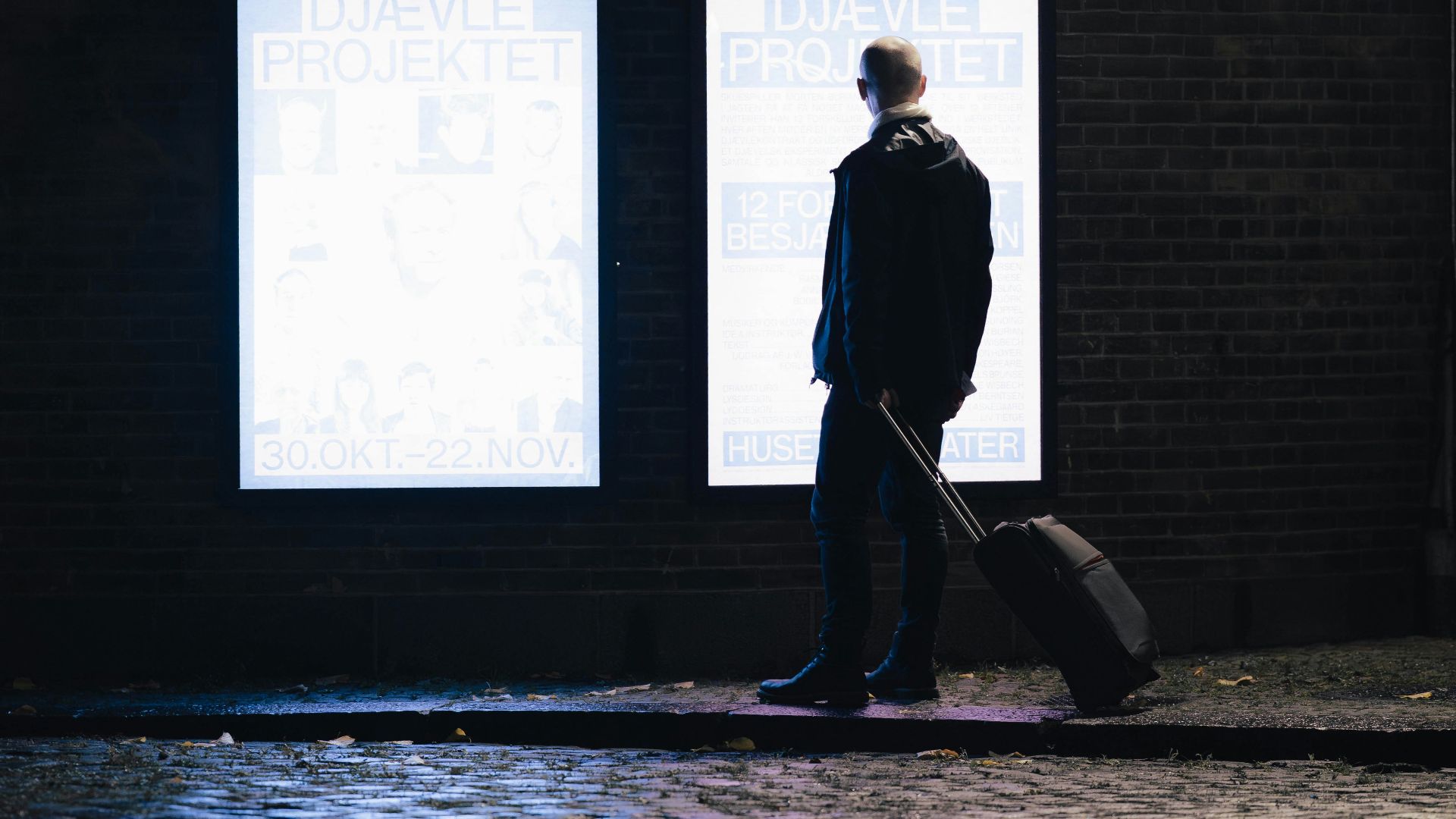Man with suitcase walks past illuminated posters at night
