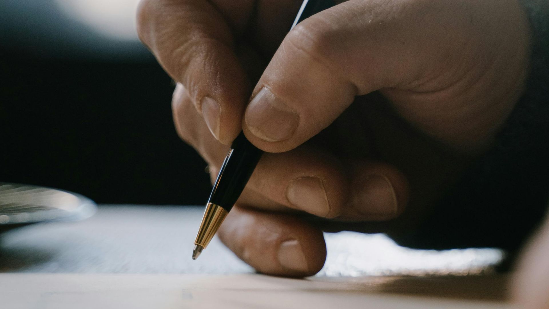Detail shot of a hand holding a pen, writing on paper with blurred background.