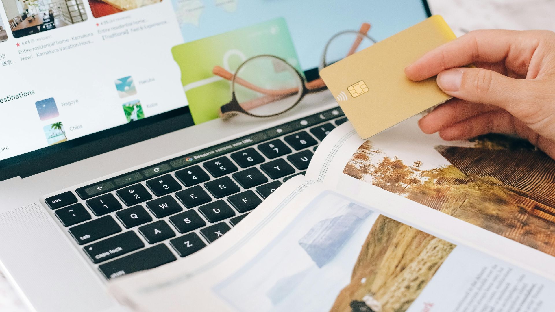 Hands holding credit card over laptop and magazine for online shopping and travel planning.