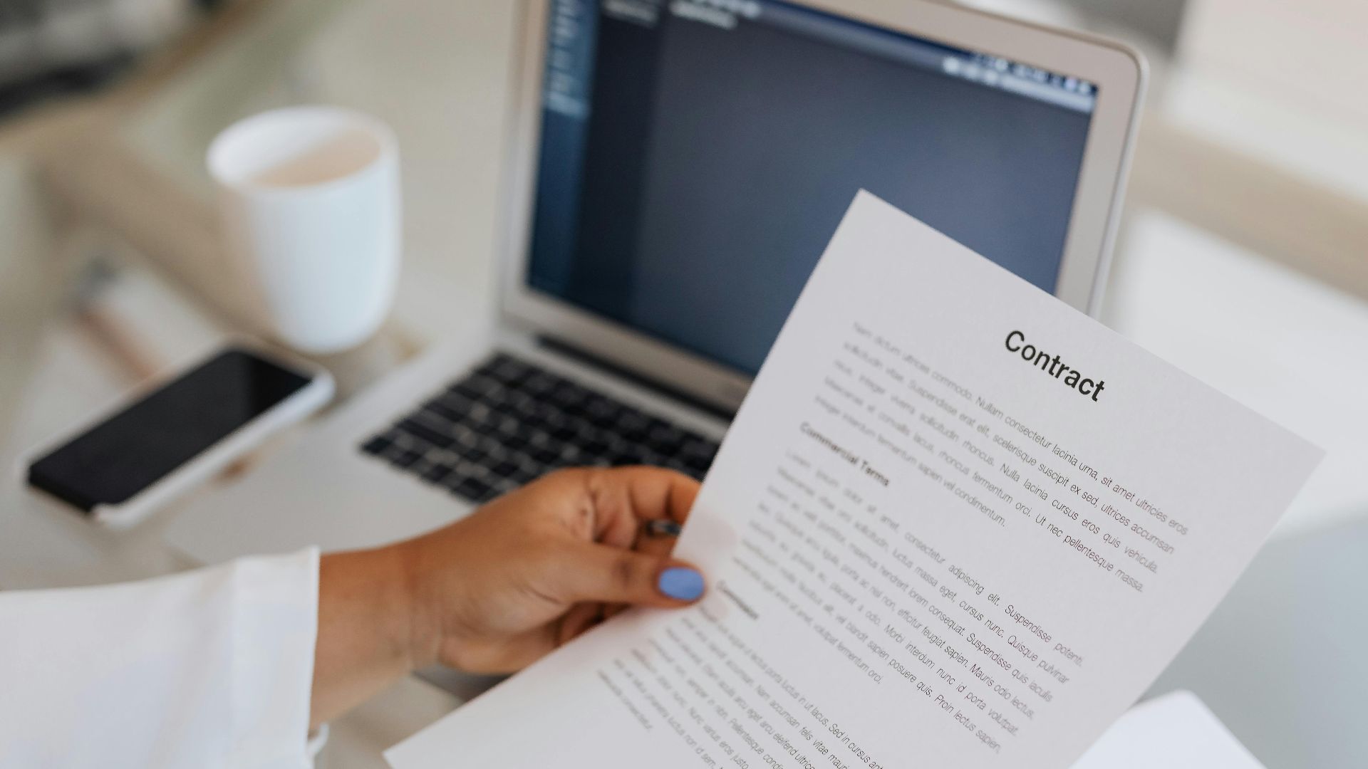 Close-up of a person holding a contract document next to a laptop during a work session.