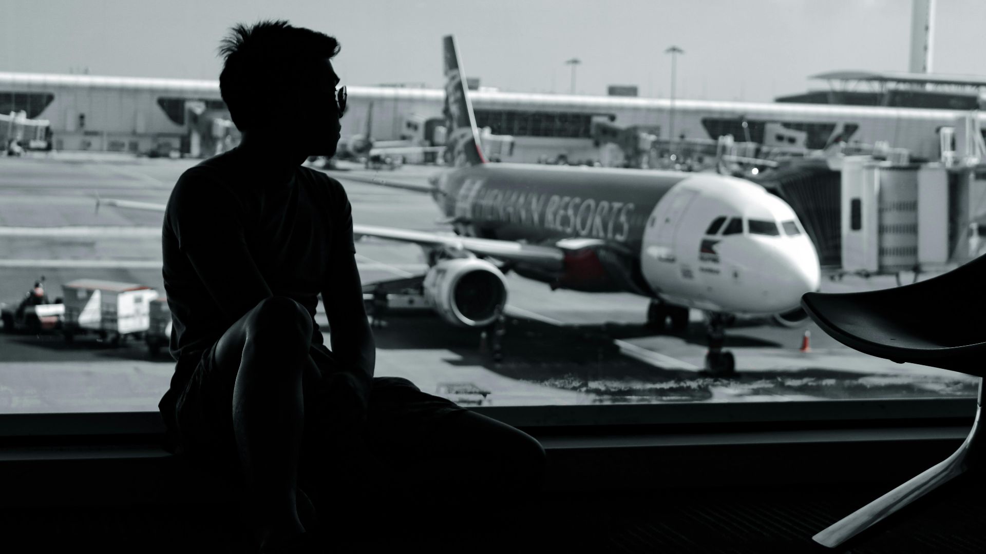 A silhouetted man sits in an airport terminal, viewing an airplane on the tarmac.