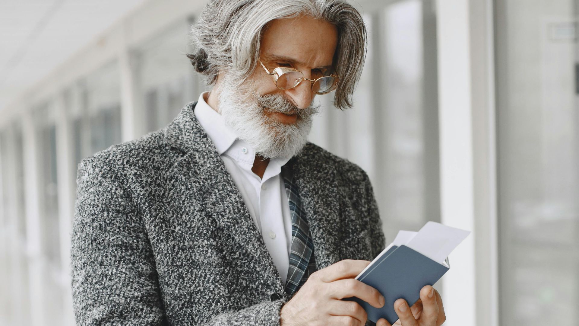Elegant senior businessman in a suit holding a passport indoors.