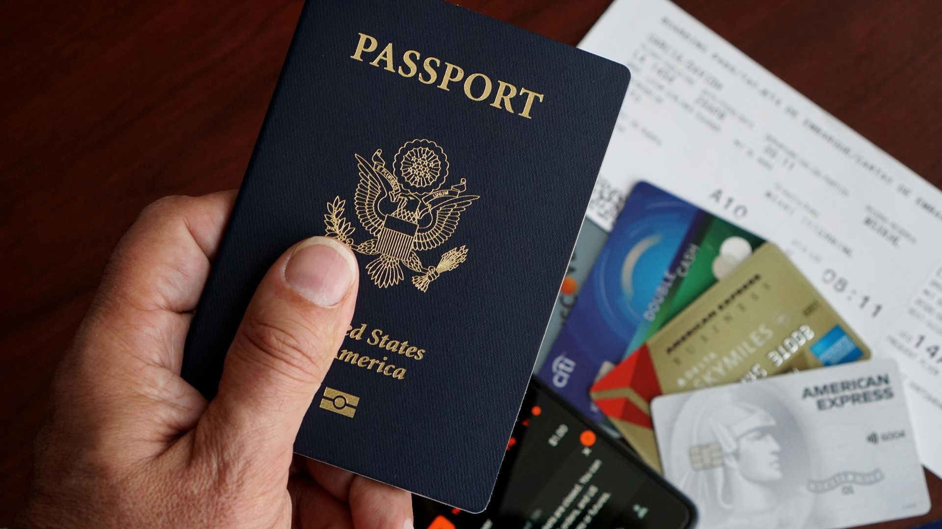 A close-up of a US passport with credit cards, tickets, and a mobile phone on a table.