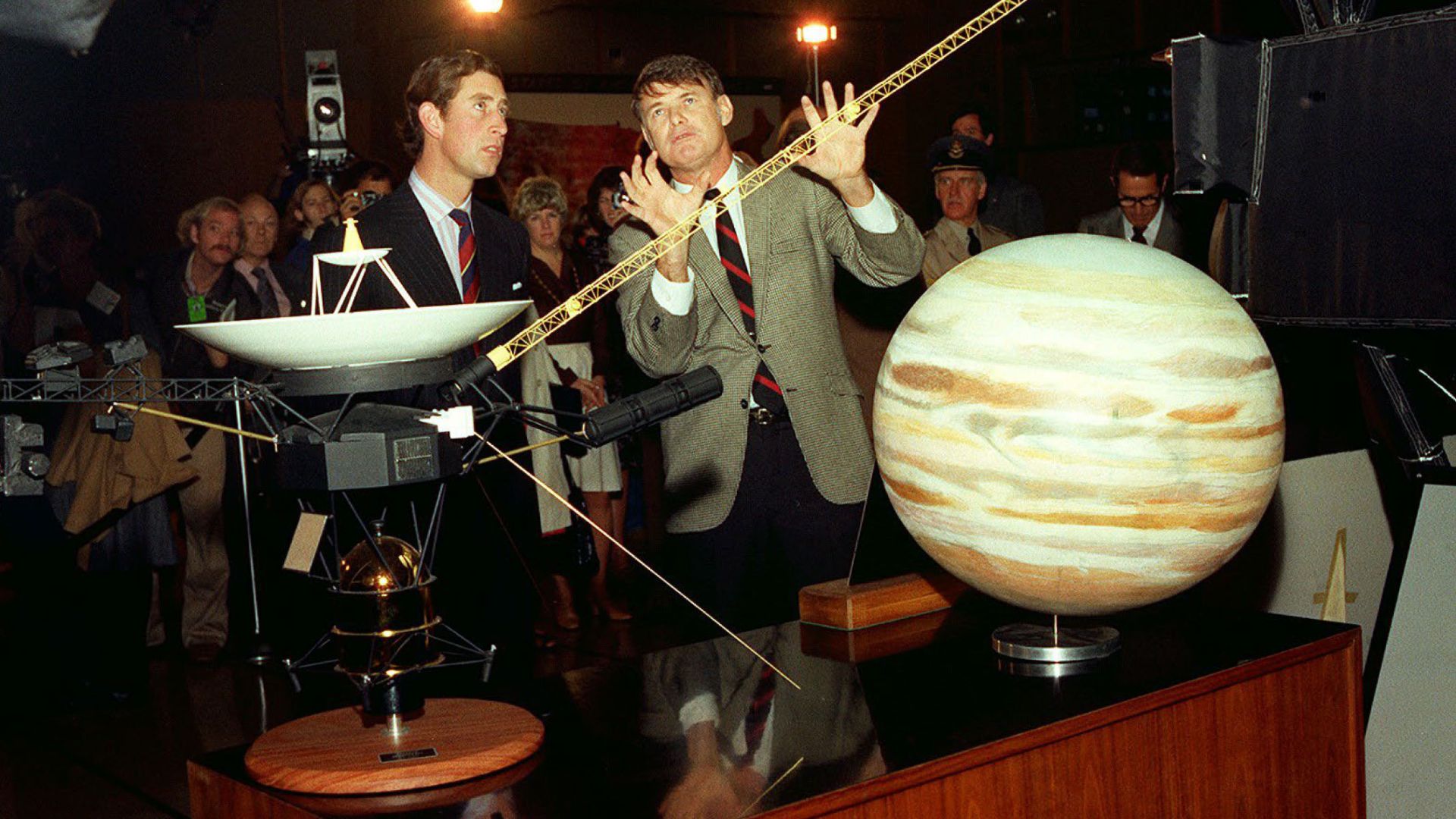 Prince Charles of Wales (now King of the United Kingdom of Great Britain and Northern Ireland) is pictured here during a visit to JPL on October 27, 1977. He is pictured here in mid-conversation with staff while standing in front of a model of the Voyager spacecraft