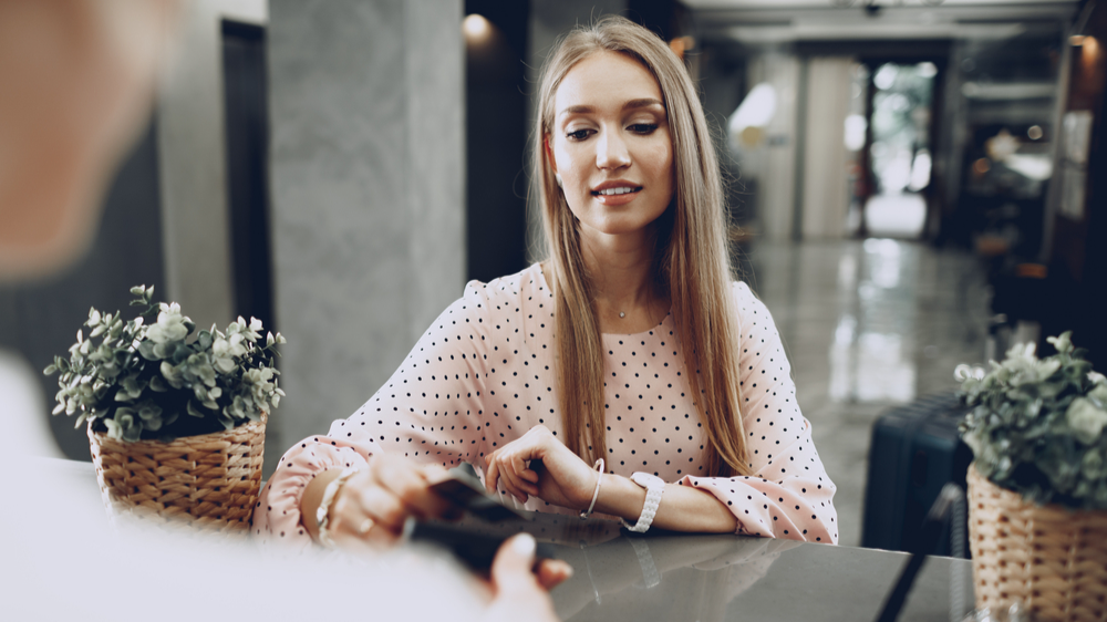Young beautiful woman hotel guest paying for her stay with credit card at front desk