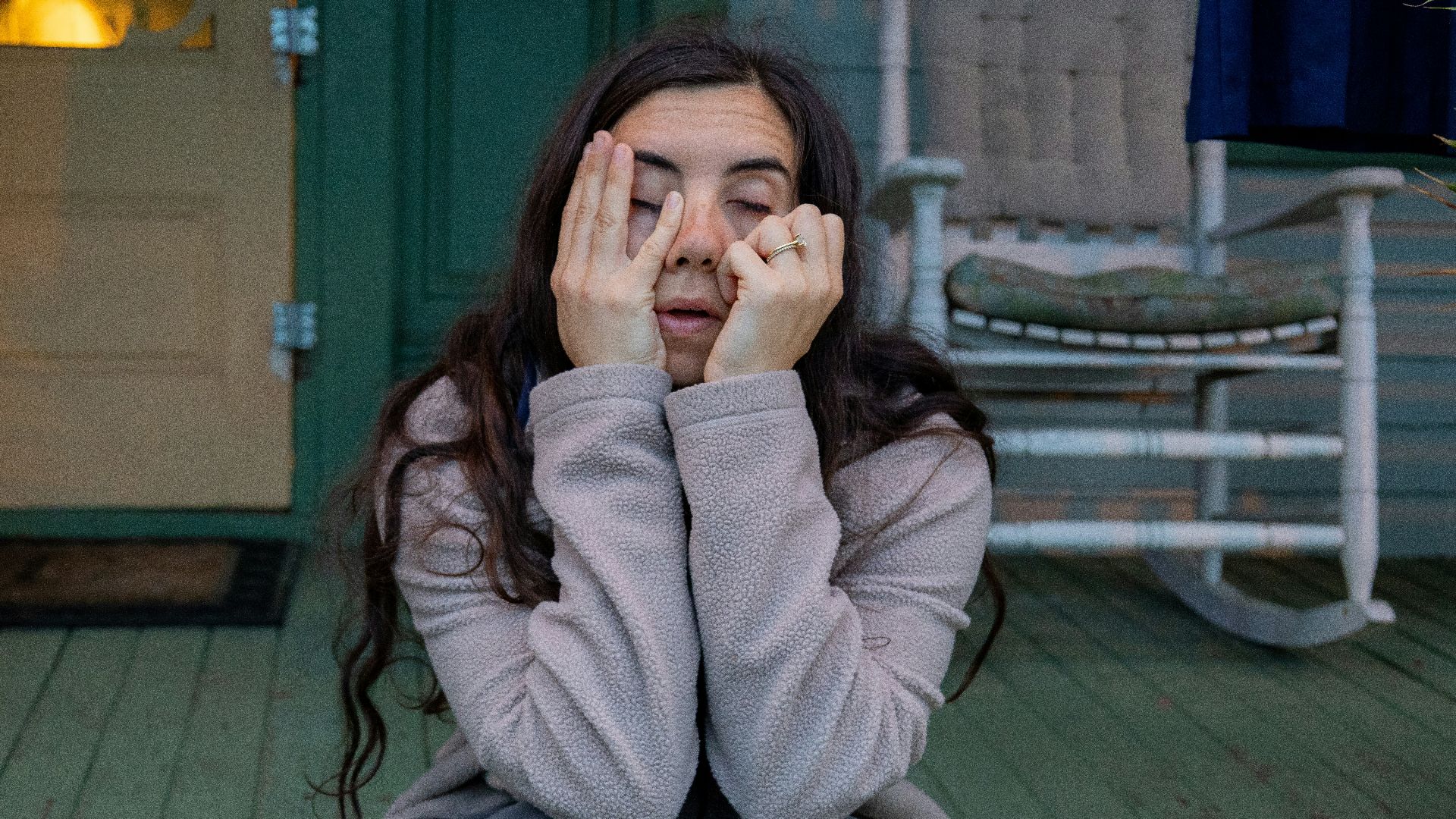 a woman sitting on a porch covering her eyes