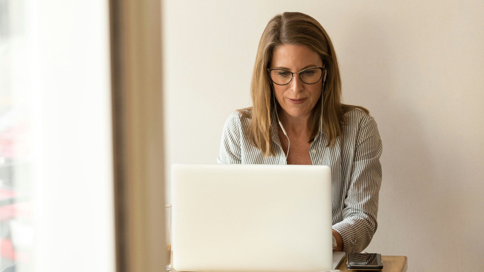 woman wearing grey striped dress shirt sitting down near brown wooden table in front of white laptop computer