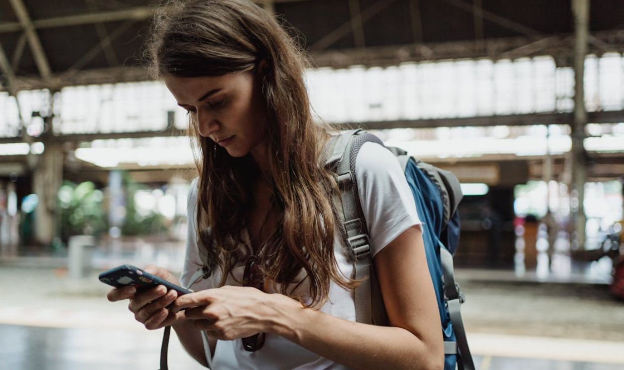 A young woman checks her smartphone while traveling at a train station.