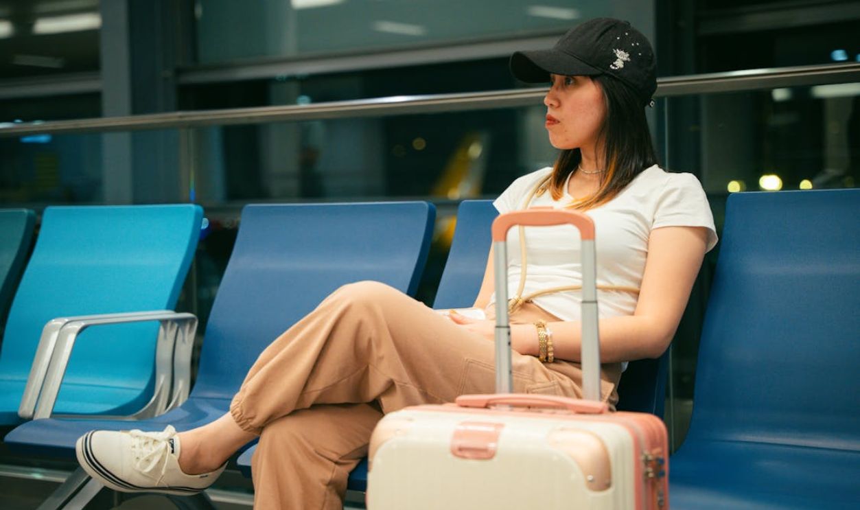 Young woman sitting at an airport terminal with luggage, looking thoughtful and waiting for her flight.