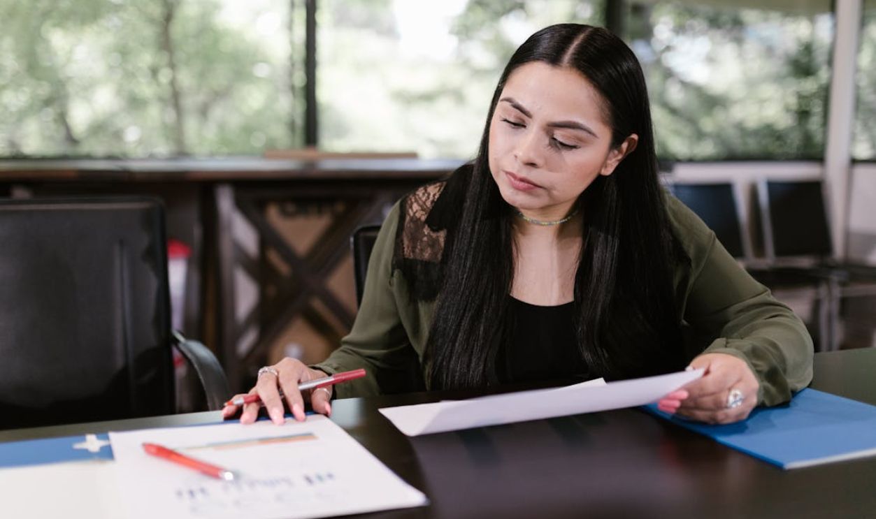 Professional woman in office setting studying documents with concentration.
