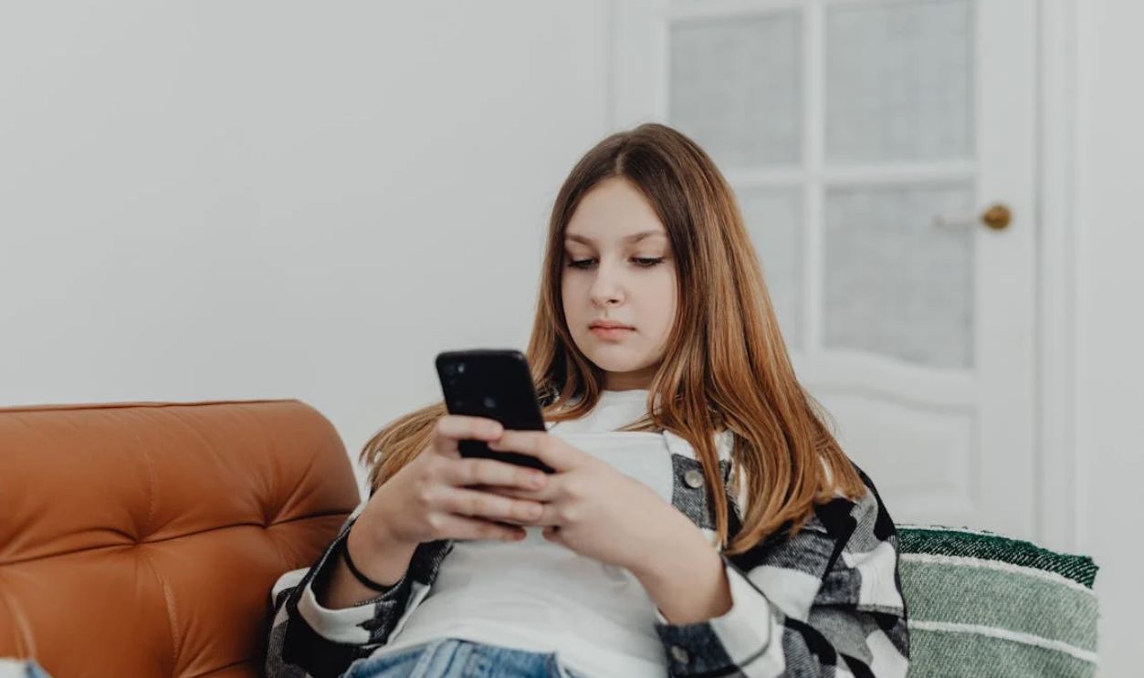 Teenage girl using smartphone while lounging on a sofa indoors.